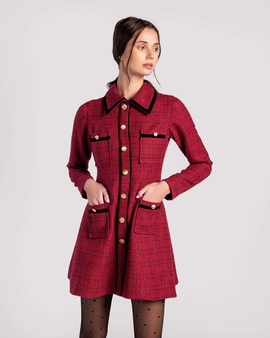 Woman wearing a red tweed dress with gold buttons and black trim, posing in studio