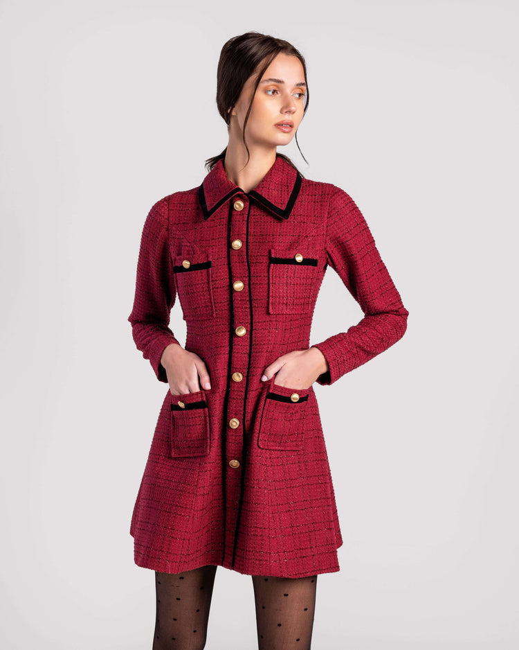 Woman wearing a red tweed dress with gold buttons and black trim, posing in studio
