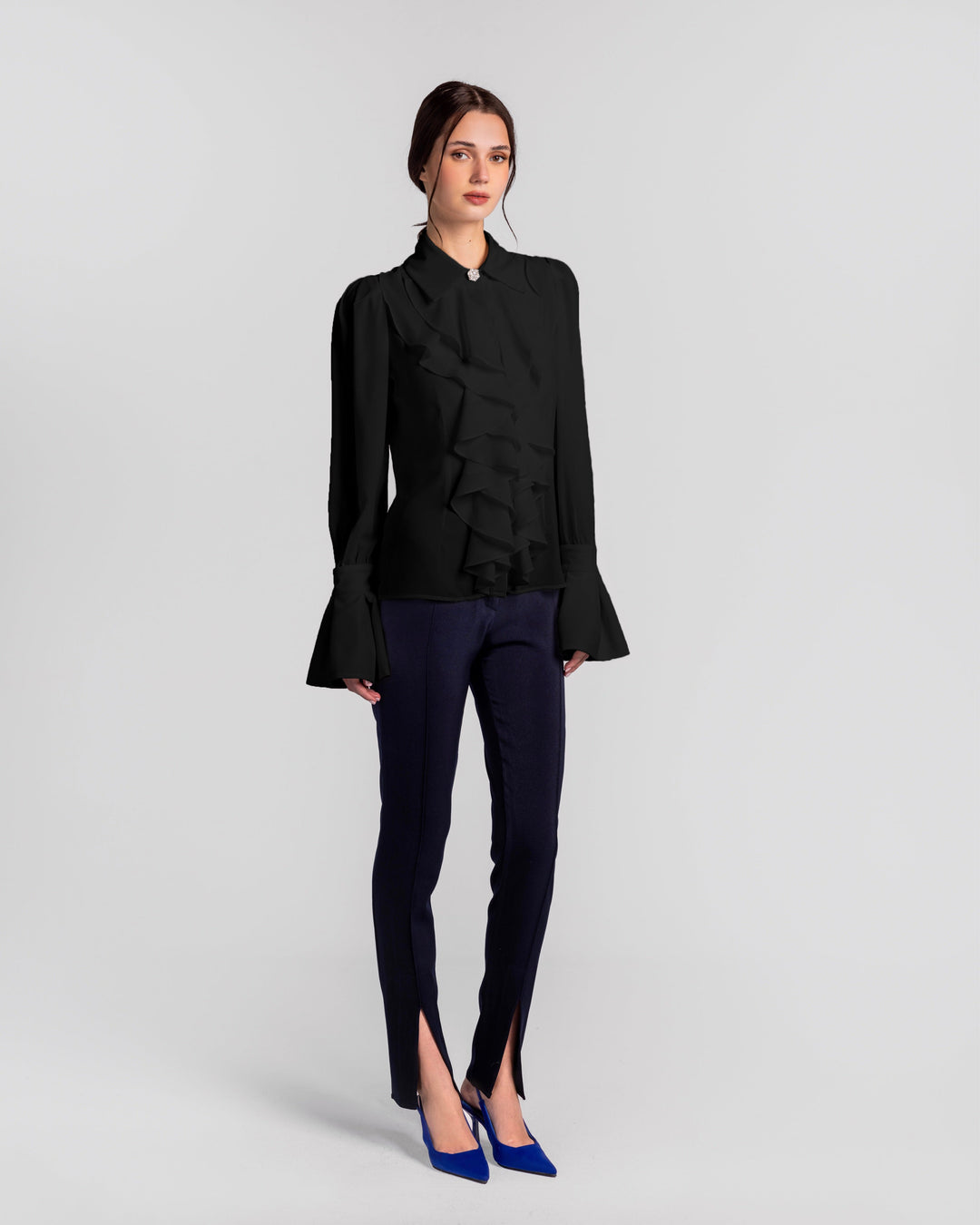 Woman wearing a black ruffle blouse with flared sleeves, navy slit pants, and blue heels