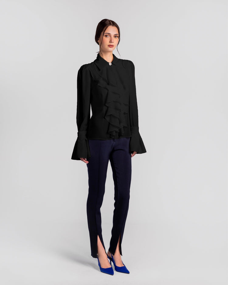 Woman wearing a black ruffle blouse with flared sleeves, navy slit pants, and blue heels