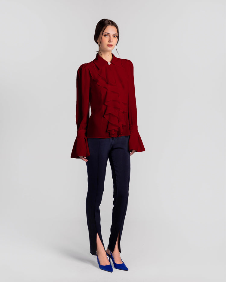 Woman in a red ruffle blouse, navy slim-fit split hem pants, and blue heels, studio background
