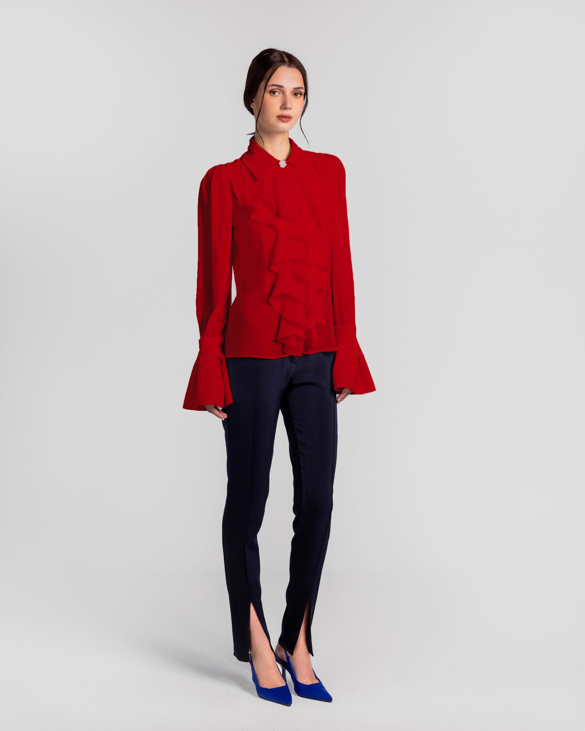Woman in red ruffled blouse with flared cuffs, navy pants with front slits, and blue heels