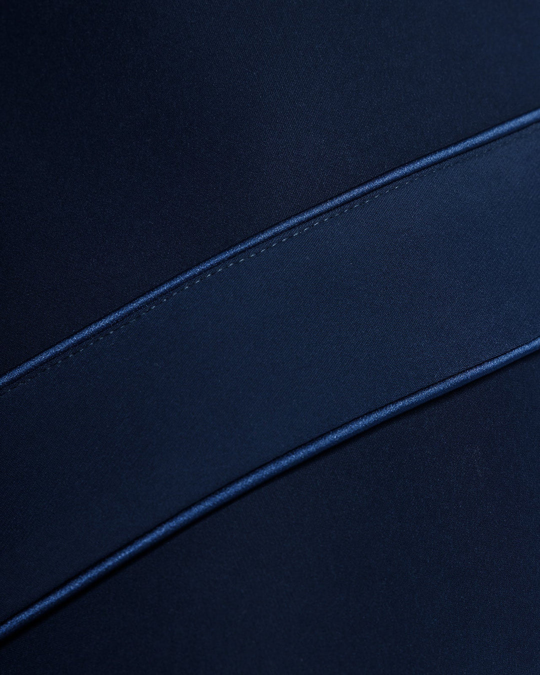 Close-up of dark blue satin dress fabric with diagonal seam detail