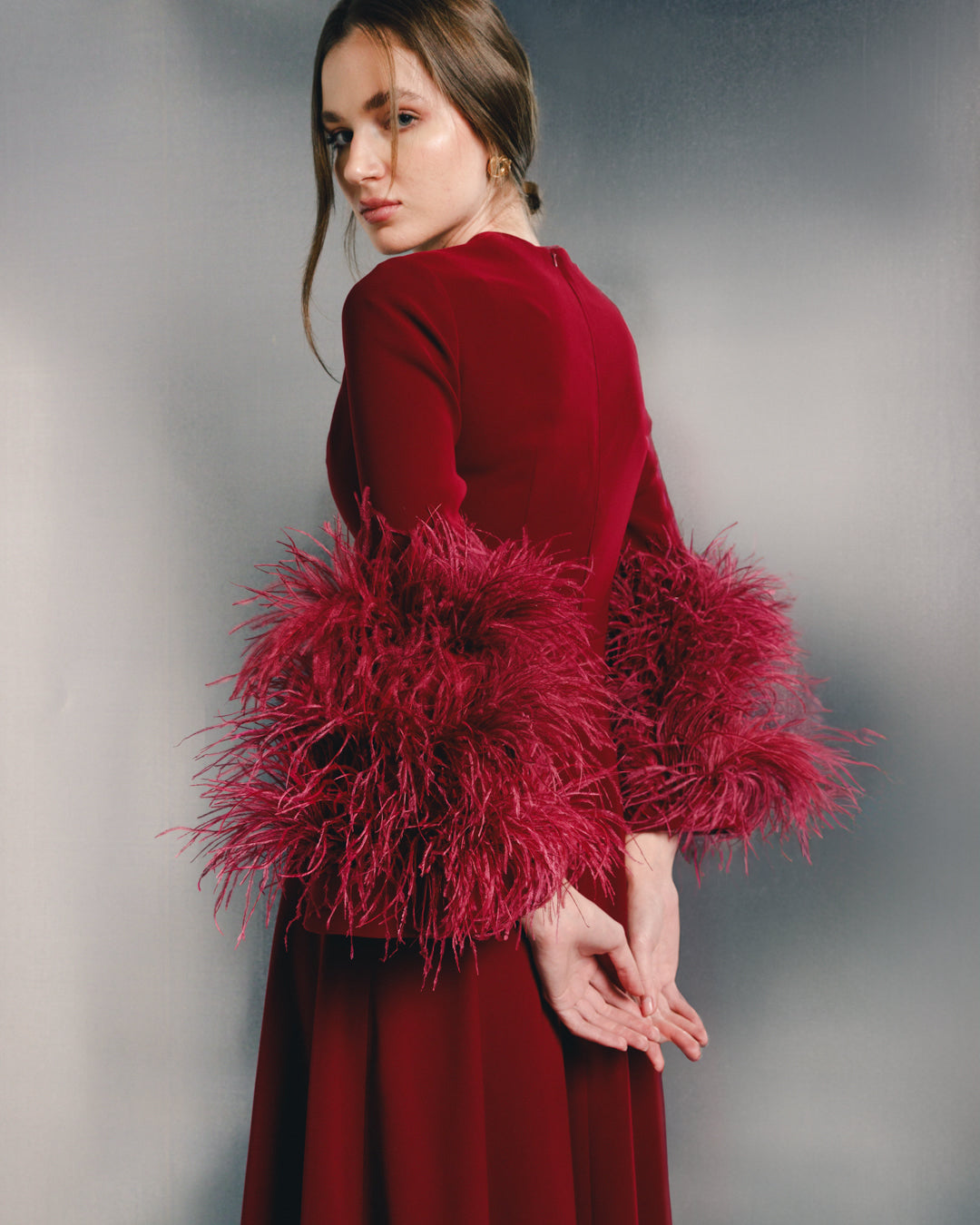 Woman in elegant burgundy dress with dramatic feathered sleeves, fashion studio setting