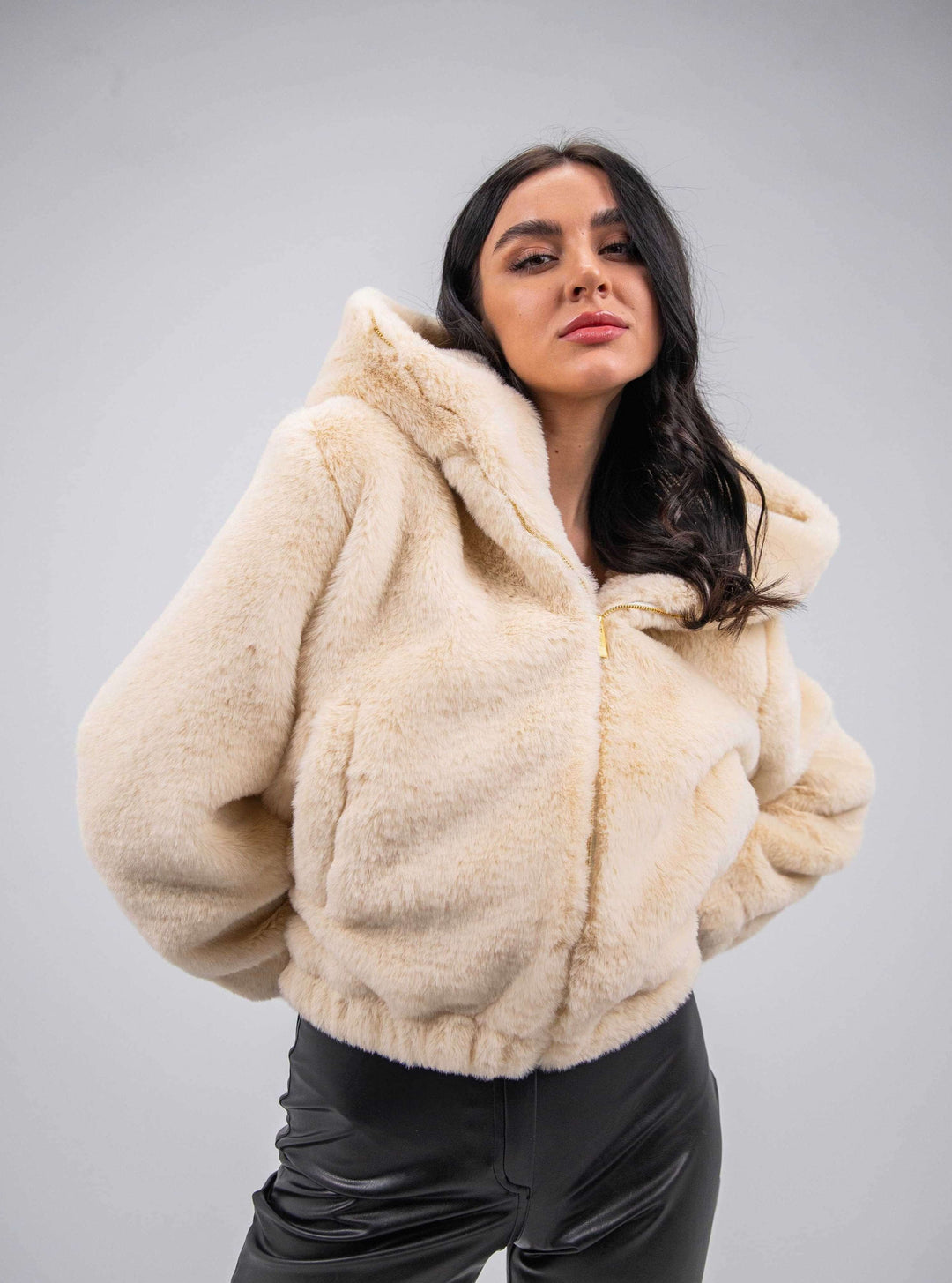 Woman wearing a beige faux fur hooded jacket and black leather pants, fashion studio shot