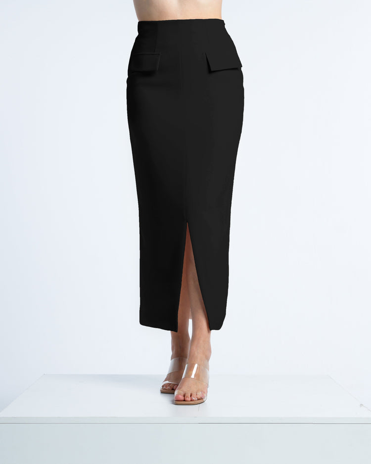 High-waisted black midi pencil skirt with front slit and pocket flaps, worn with clear heels.