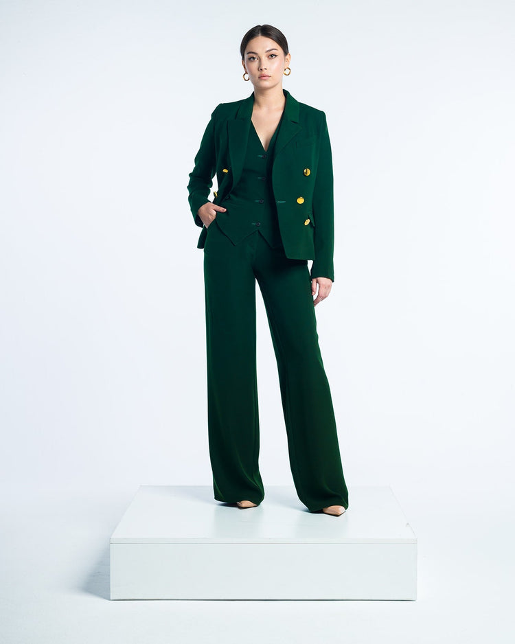Woman wearing a dark green pantsuit with gold buttons, standing on white platform