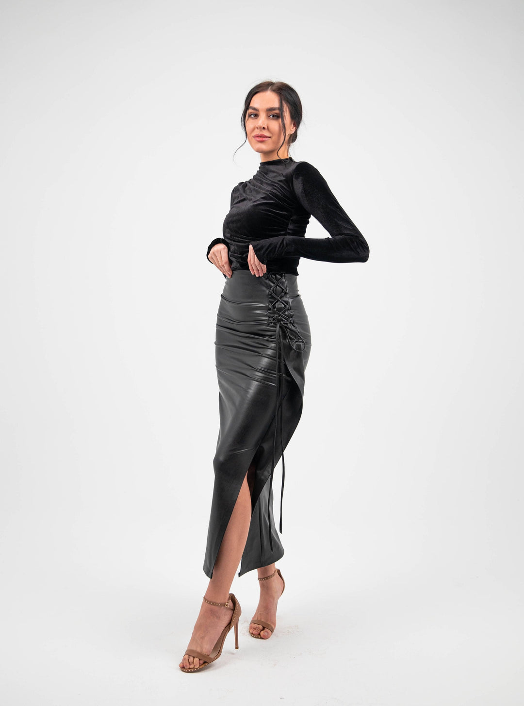 Woman in black velvet long sleeve top and high-waisted faux leather skirt with lace-up side slit
