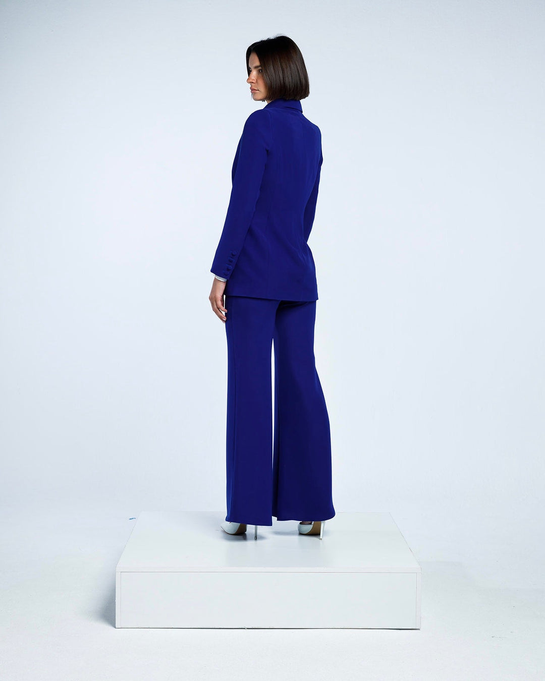Woman wearing royal blue tailored suit with blazer and wide-leg pants, standing on platform