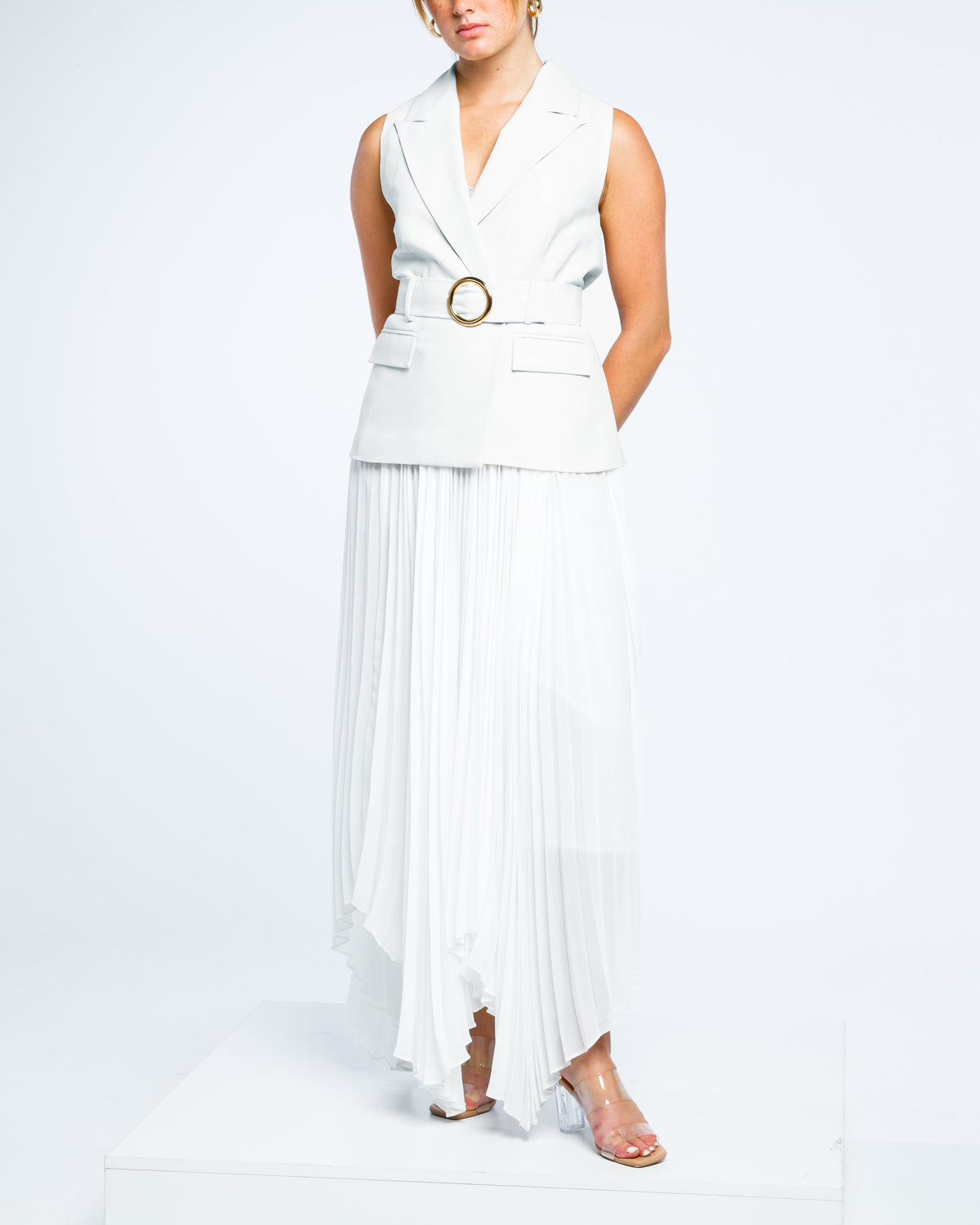 Sleeveless white belted blazer dress with pleated chiffon skirt and clear heels