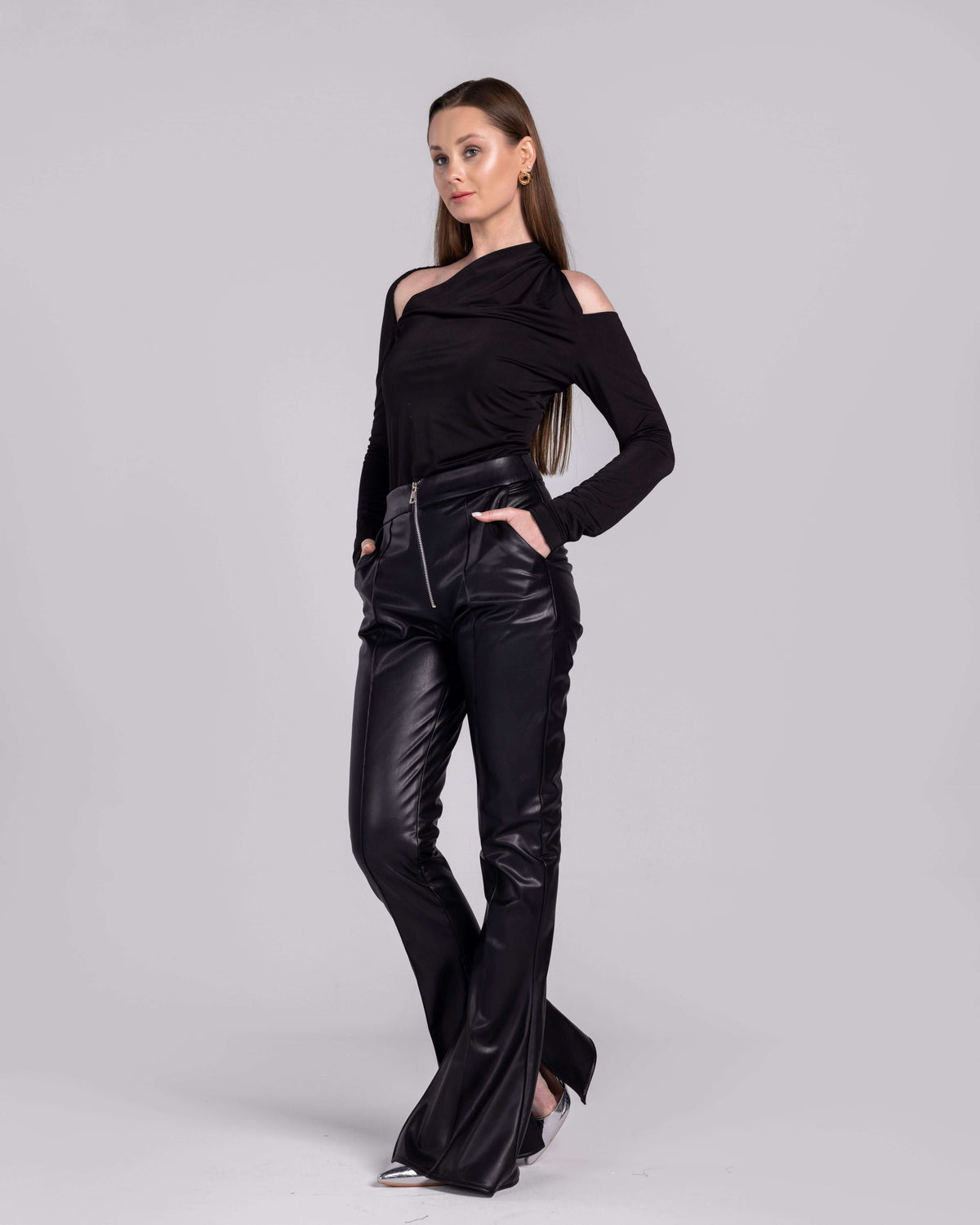 Woman modeling black cutout shoulder top and high-waisted leather pants against a plain background