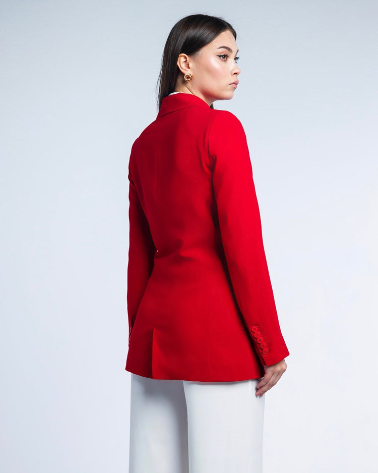 Woman in elegant red blazer and white trousers, standing against a plain background