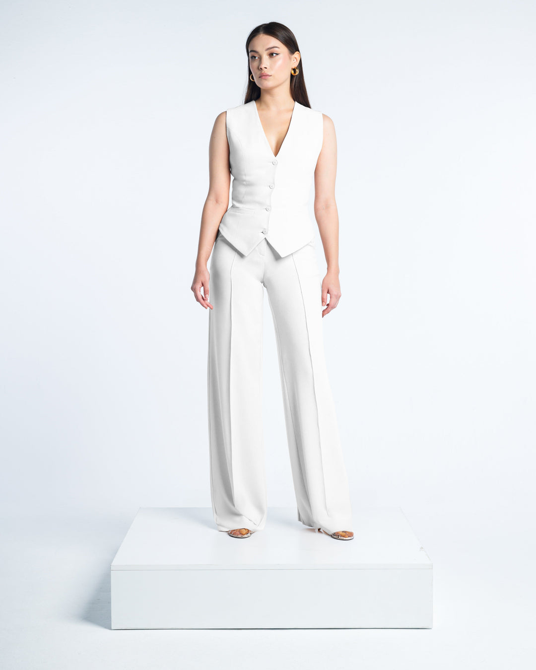 Woman in white tailored vest and wide-leg suit pants standing on platform, elegant fashion