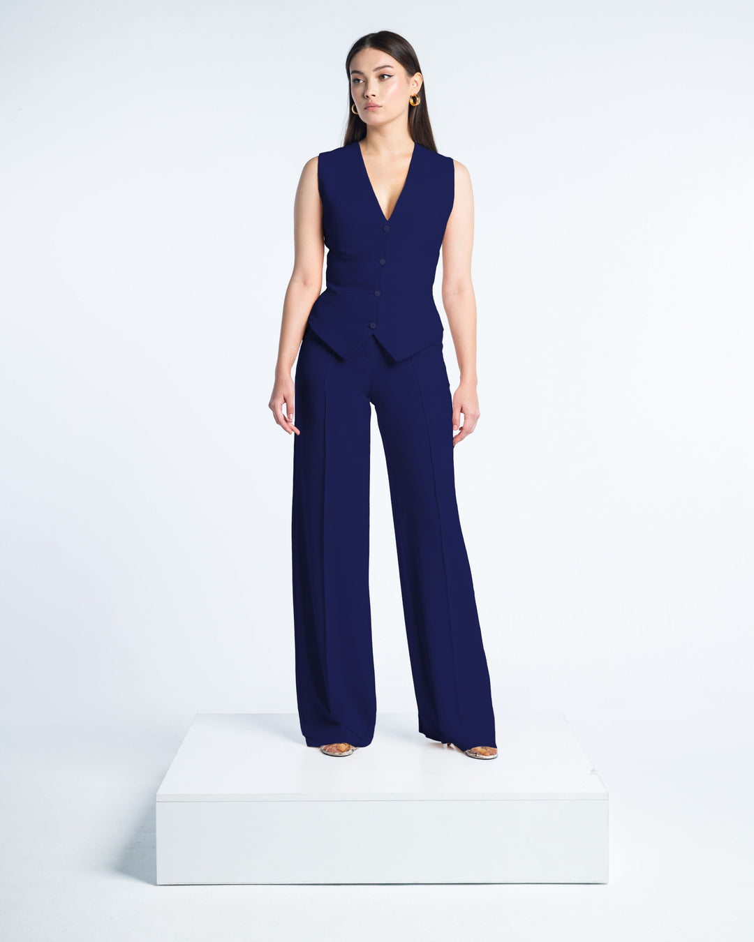 Woman wearing sleeveless navy blue vest and wide-leg suit pants, standing on platform.