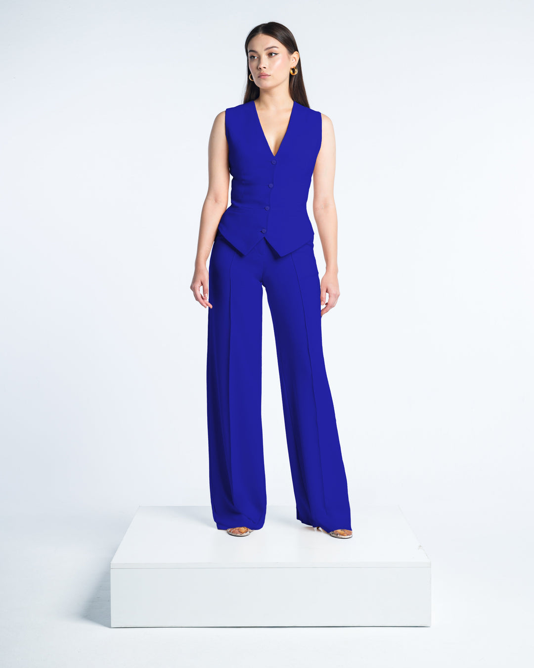 Woman wearing royal blue sleeveless vest and wide-leg pants suit set, standing on white platform