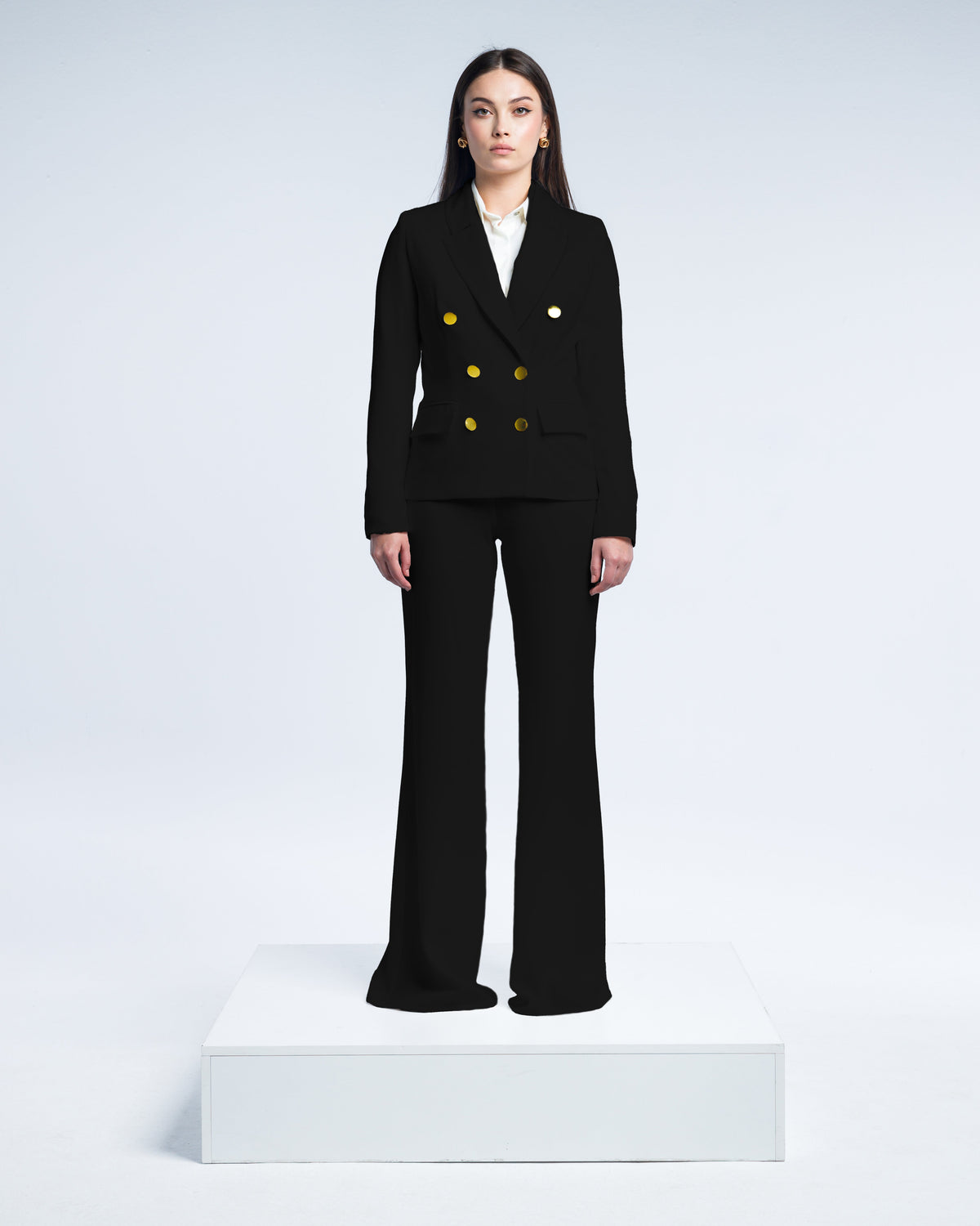 Woman wearing a tailored black suit with gold buttons, white blouse, and wide-leg pants