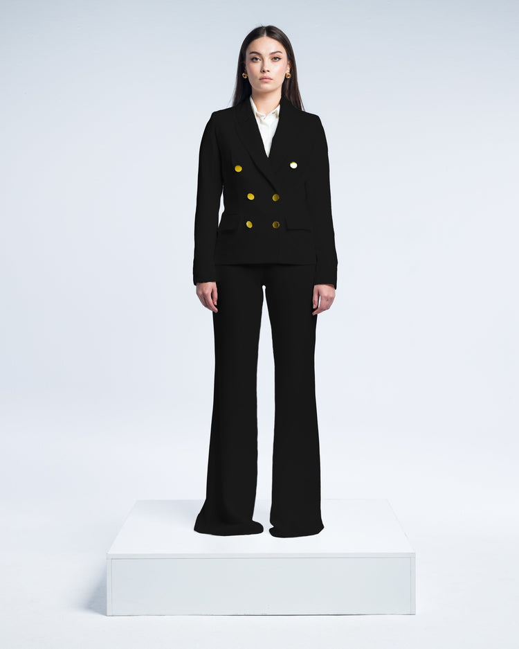Woman wearing a tailored black suit with gold buttons, white blouse, and wide-leg pants