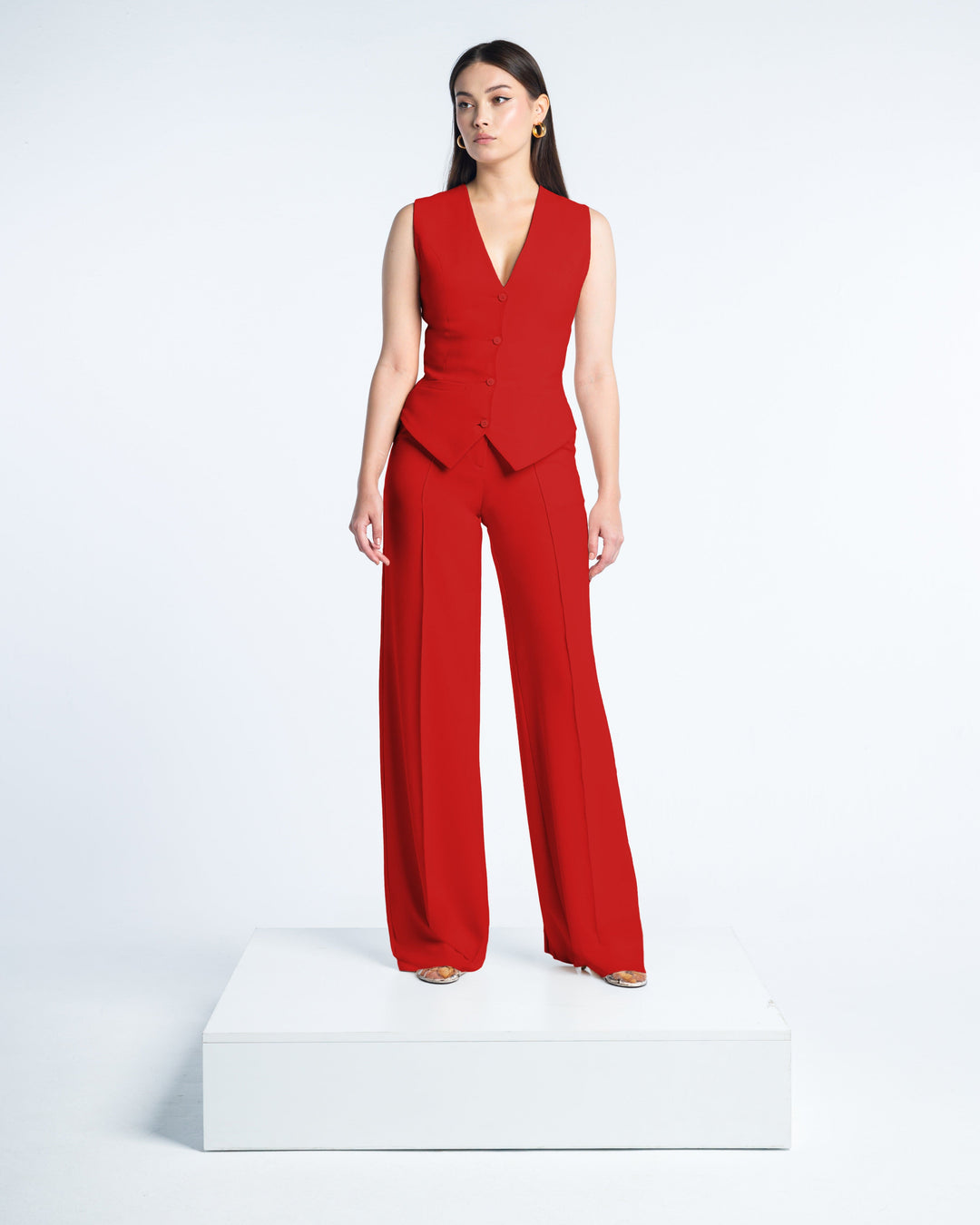 Woman modeling sleeveless red tailored suit with wide-leg pants on white background