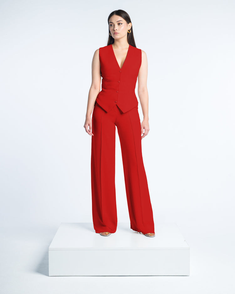 Woman modeling sleeveless red tailored suit with wide-leg pants on white background