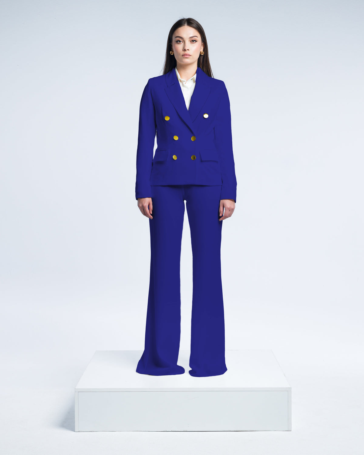 Woman wearing royal blue double-breasted suit with gold buttons, standing on white platform