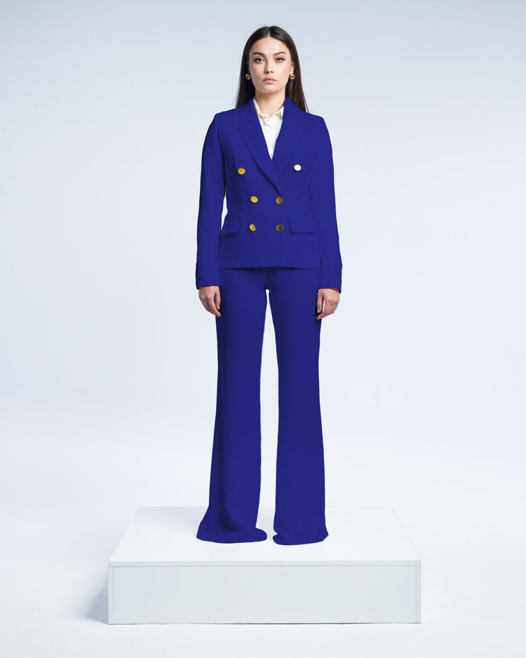 Woman wearing royal blue double-breasted suit with gold buttons, standing on white platform