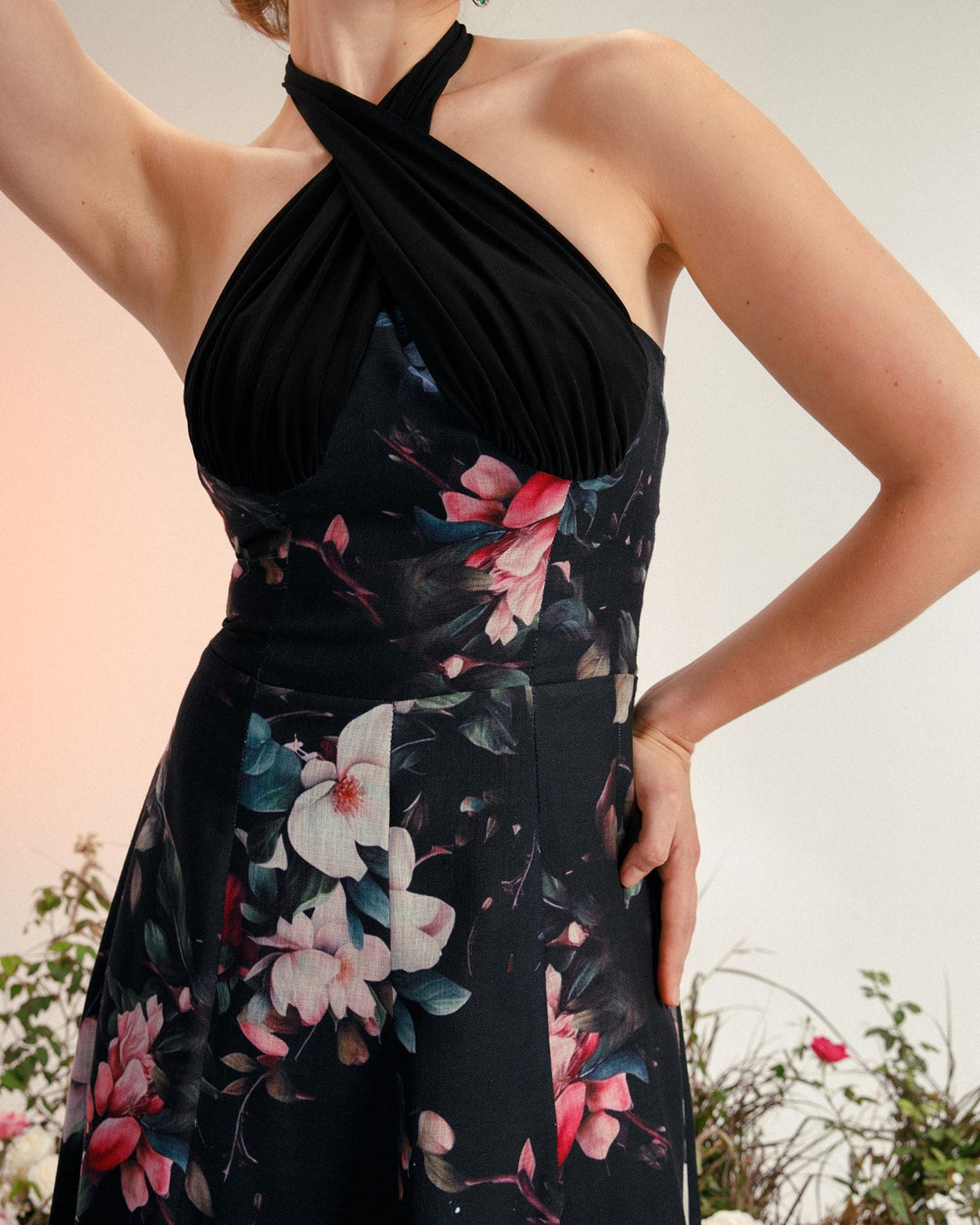 Woman wearing elegant black floral halter dress with pleated bodice and garden background
