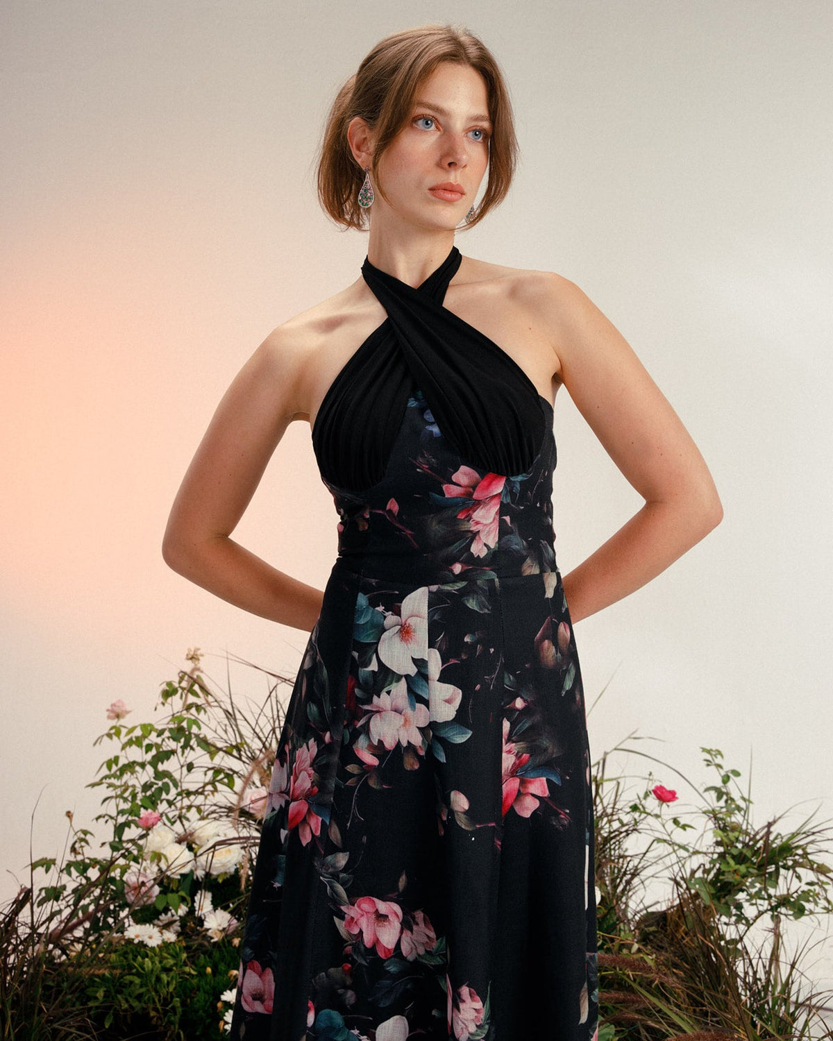 Woman wearing elegant black halter floral dress, standing indoors with flowers in background