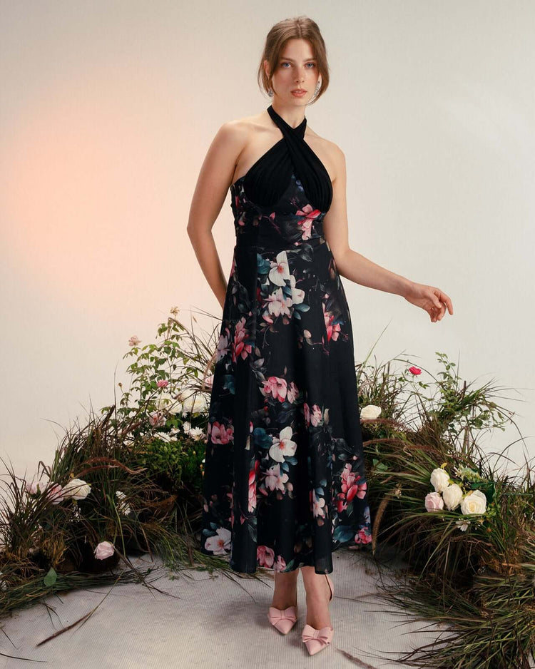 Woman wearing a black floral halter dress with pink heels, standing in a floral studio setting