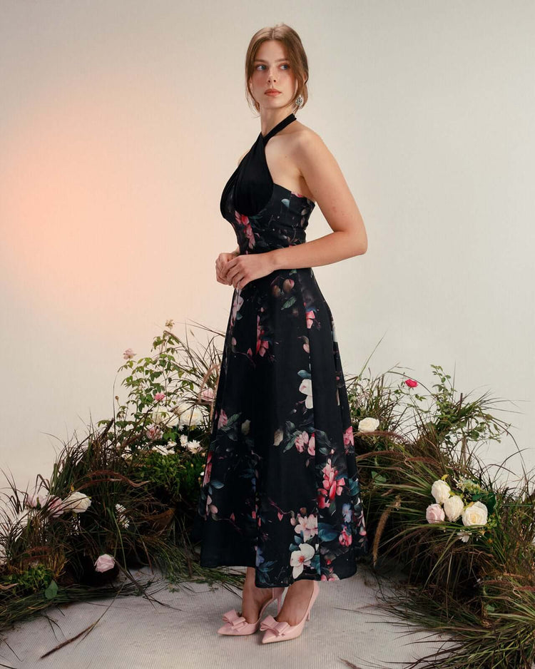 Woman wearing a black floral halter neck dress and pink bow heels standing among flowers