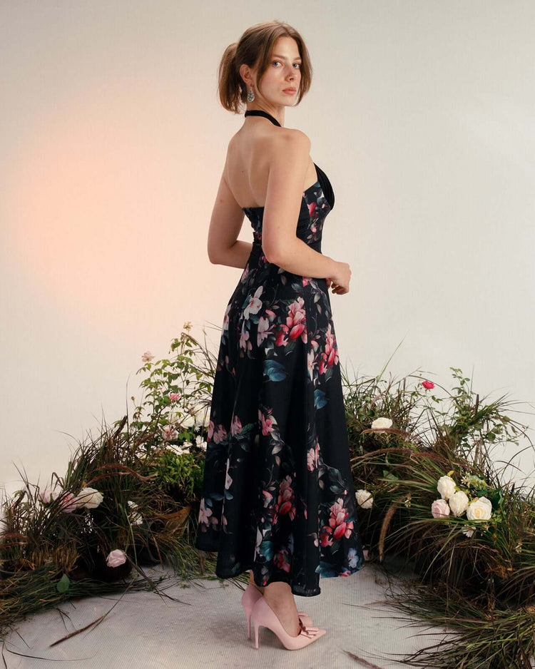 Woman in a halter-neck, floral print midi dress with pink heels standing in a floral studio setting