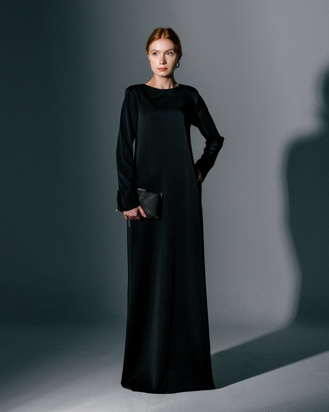 Woman wearing a long black gown dress with long sleeves, holding a black clutch