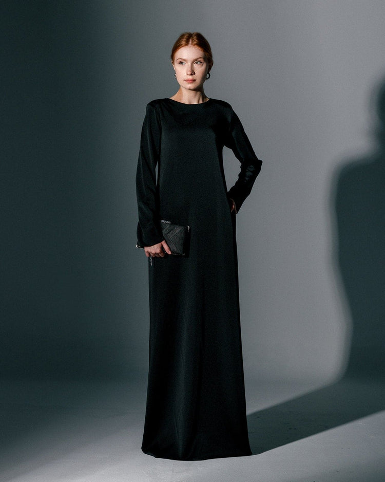 Woman wearing a long black gown dress with long sleeves, holding a black clutch
