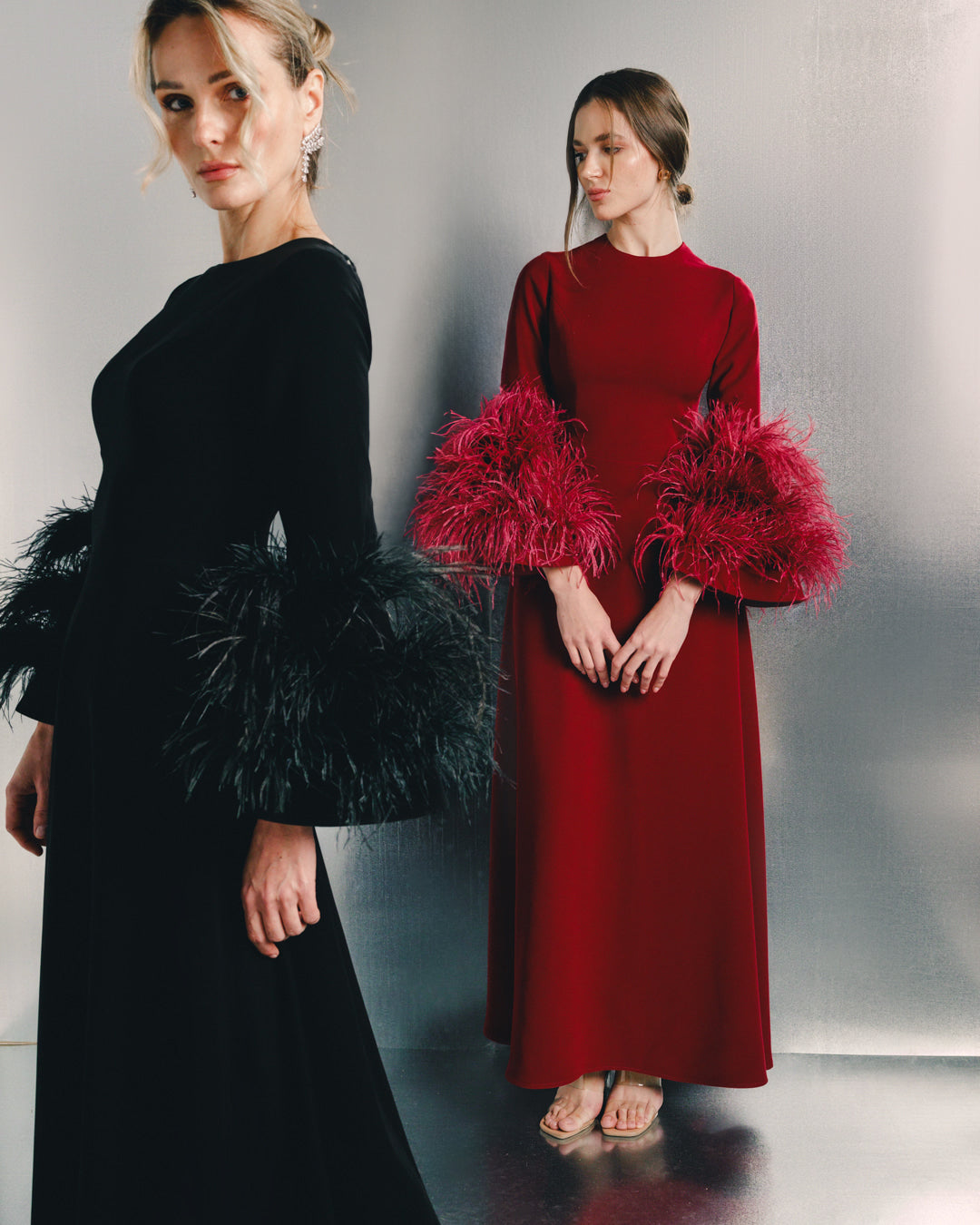Women wearing elegant black and red dresses with feathered sleeves in a modern setting