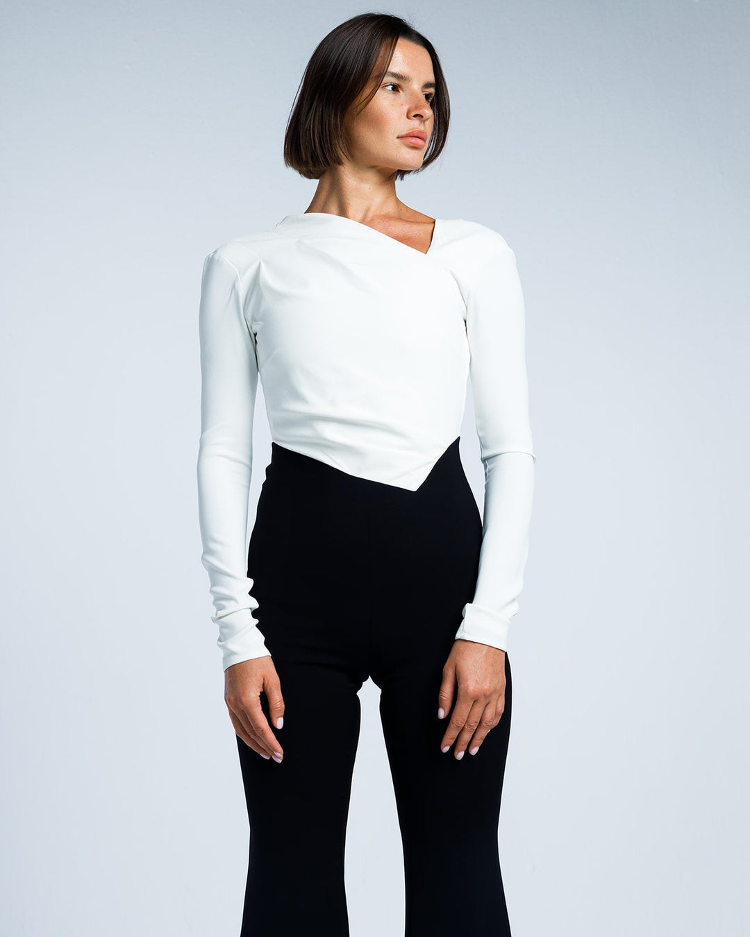 Woman modeling elegant white long-sleeve top with asymmetrical neckline and black high-waist pants