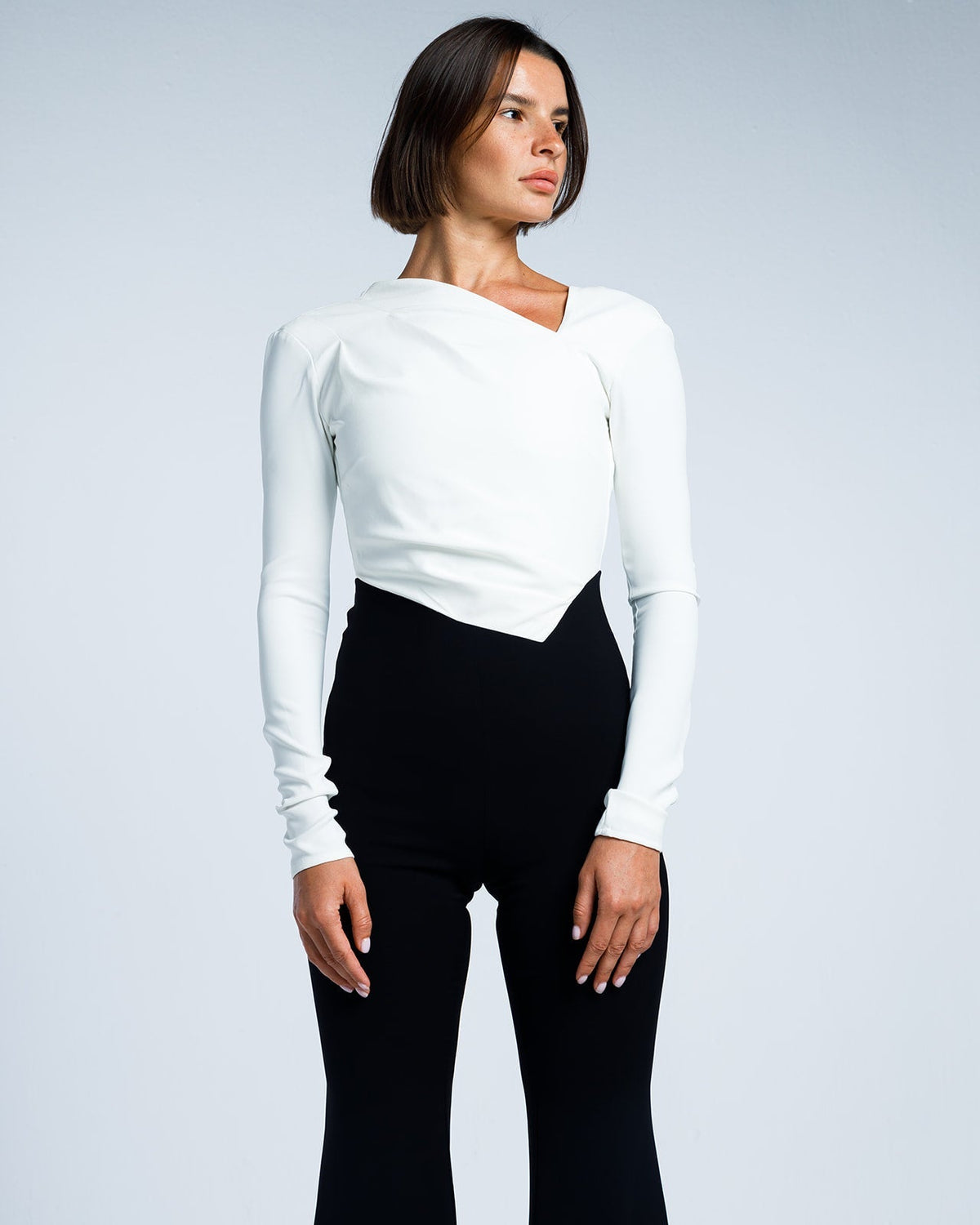 Woman modeling elegant white long-sleeve top with asymmetrical neckline and black high-waist pants