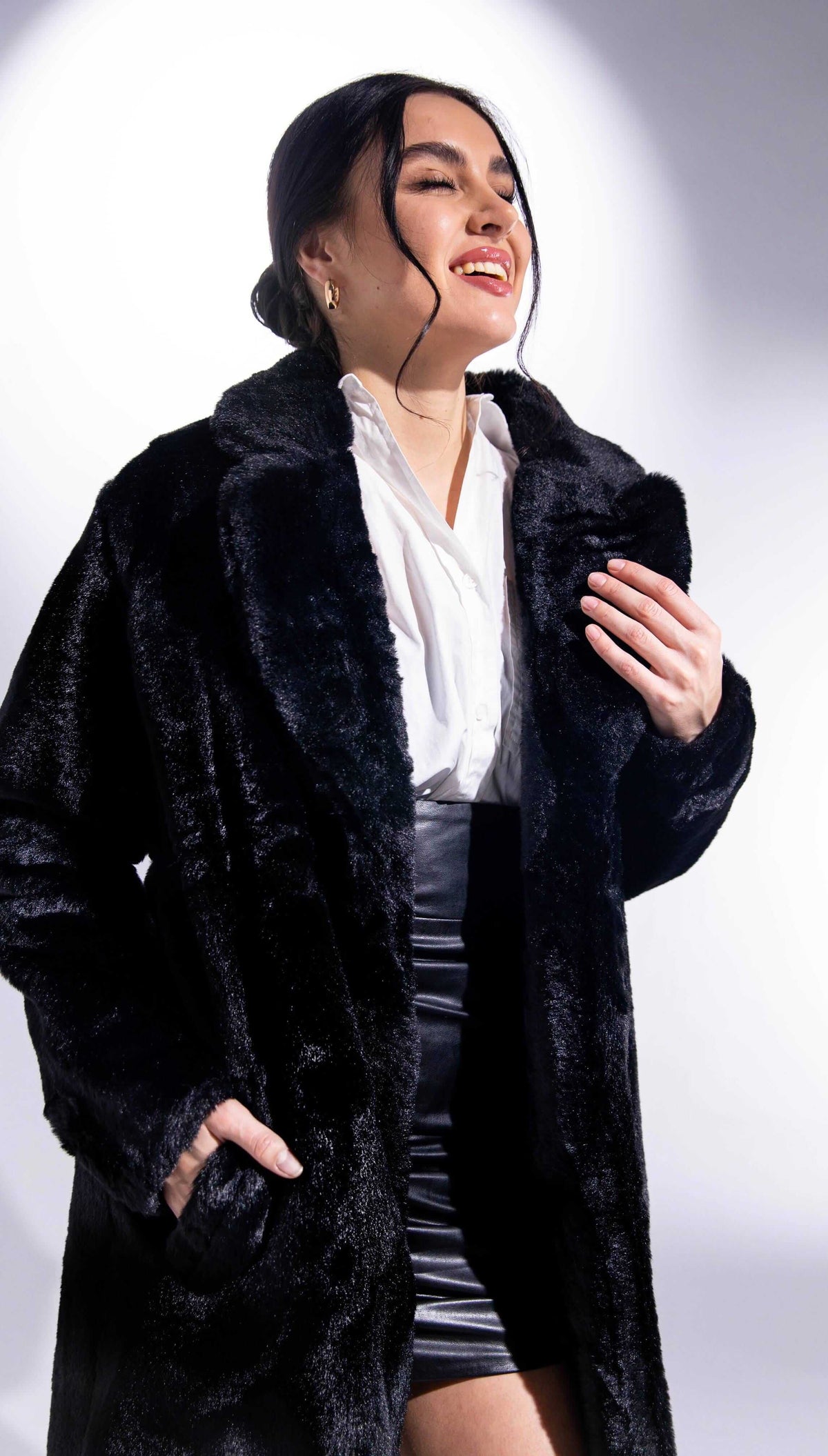 Woman in black faux fur coat and white blouse smiling in studio lighting