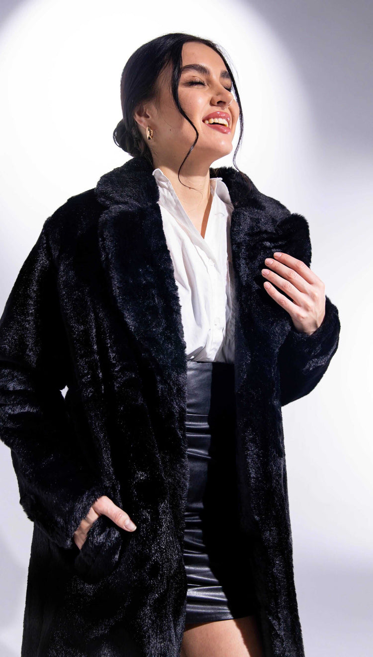 Woman in black faux fur coat and white blouse smiling in studio lighting