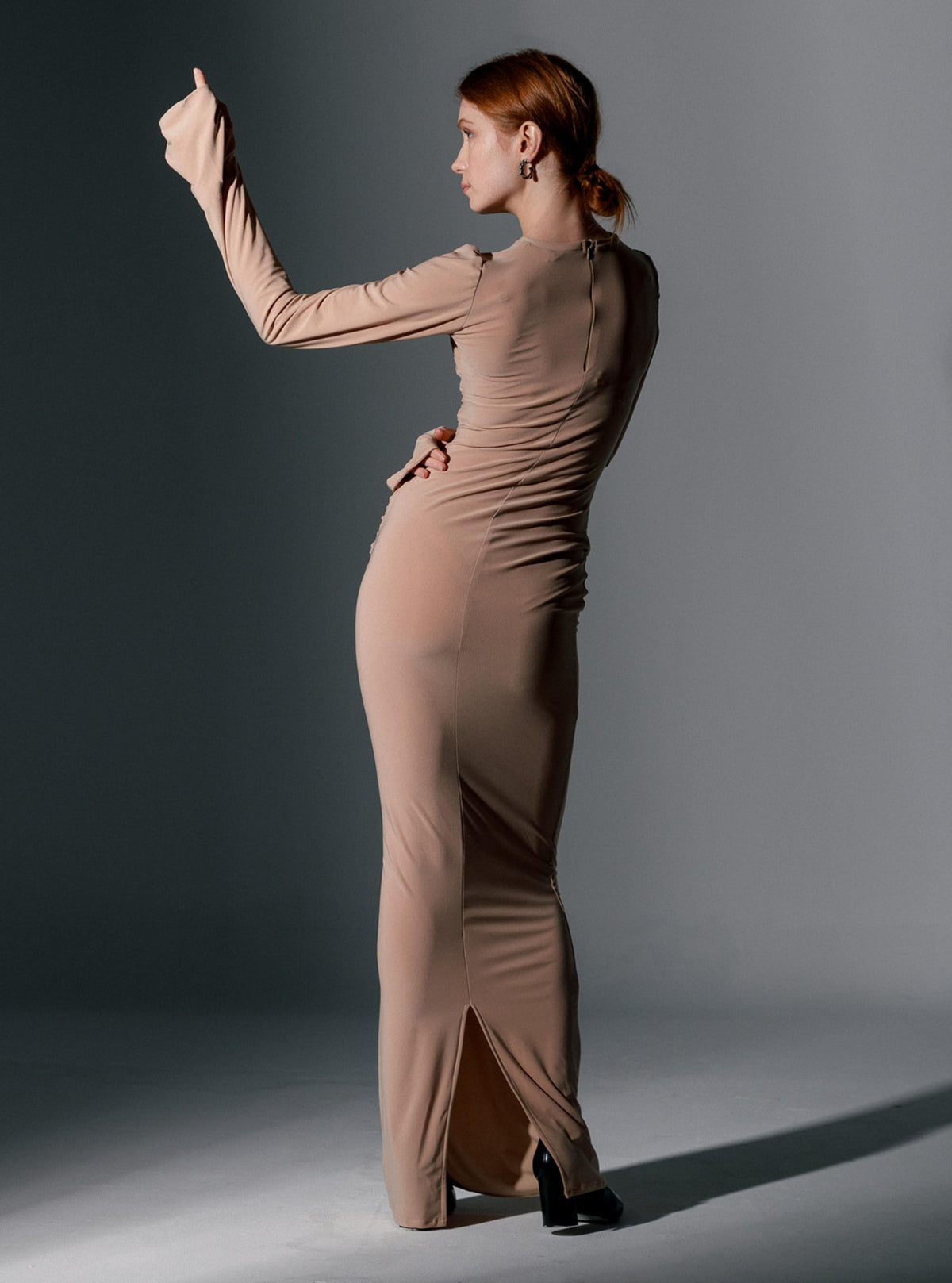 Woman in a form-fitting beige long sleeve maxi dress posing in a studio setting