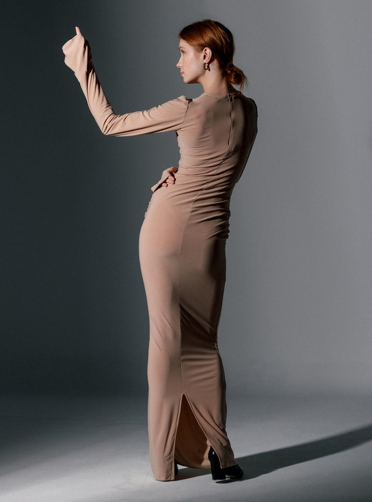 Woman in a form-fitting beige long sleeve maxi dress posing in a studio setting