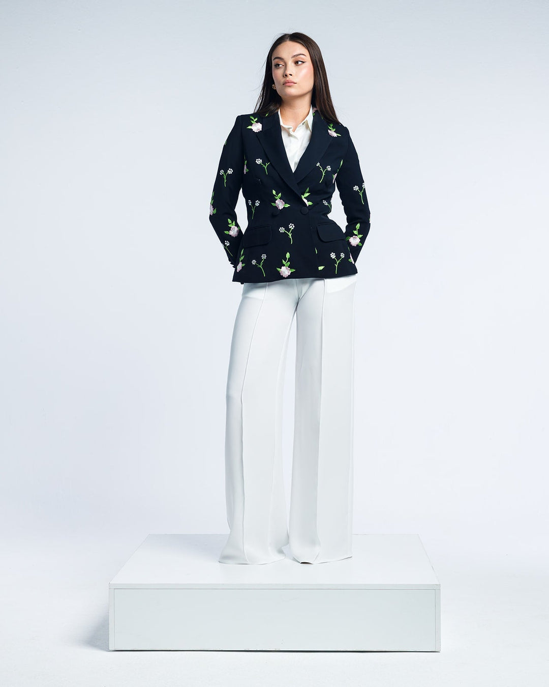 Woman in floral embroidered black blazer and white wide-leg trousers on white platform