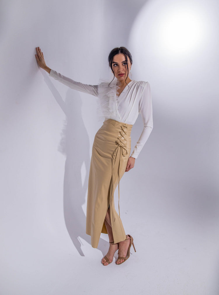 Woman in white ruffled blouse and beige high-waisted lace-up skirt, standing in studio