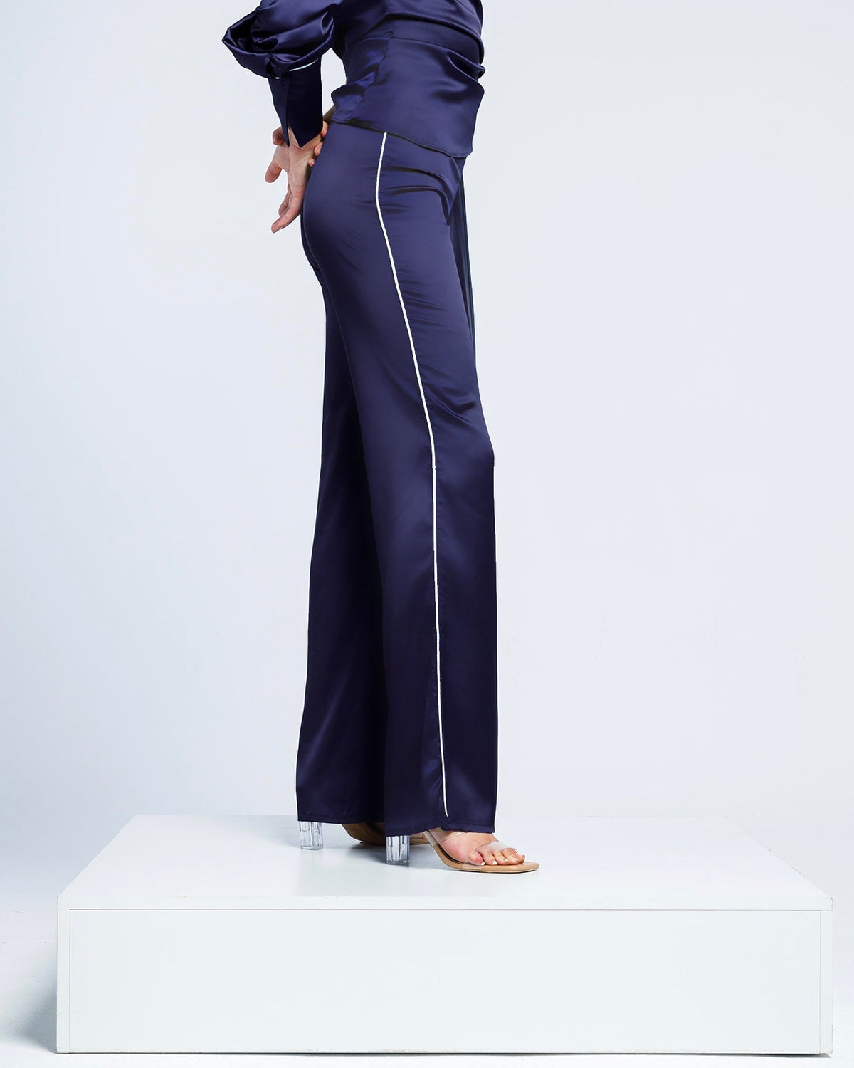 Woman wearing navy satin wide-leg pants with side piping and high heels on white platform