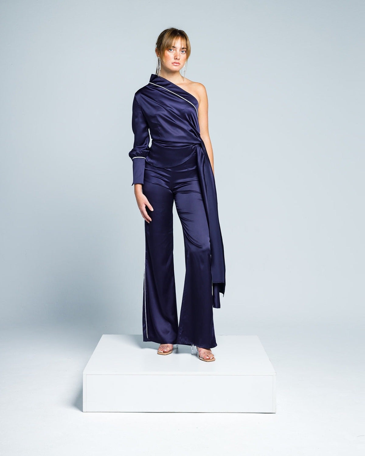 Woman in navy blue satin one-shoulder jumpsuit with flared pants and statement sash