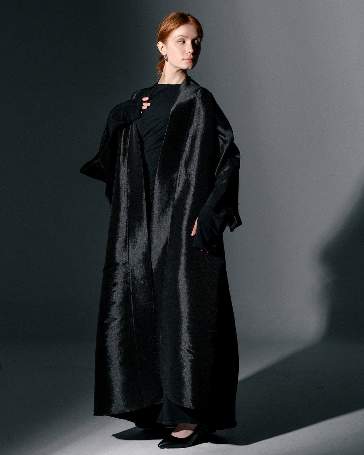 Woman wearing a black oversized satin kimono in a minimalist studio setting