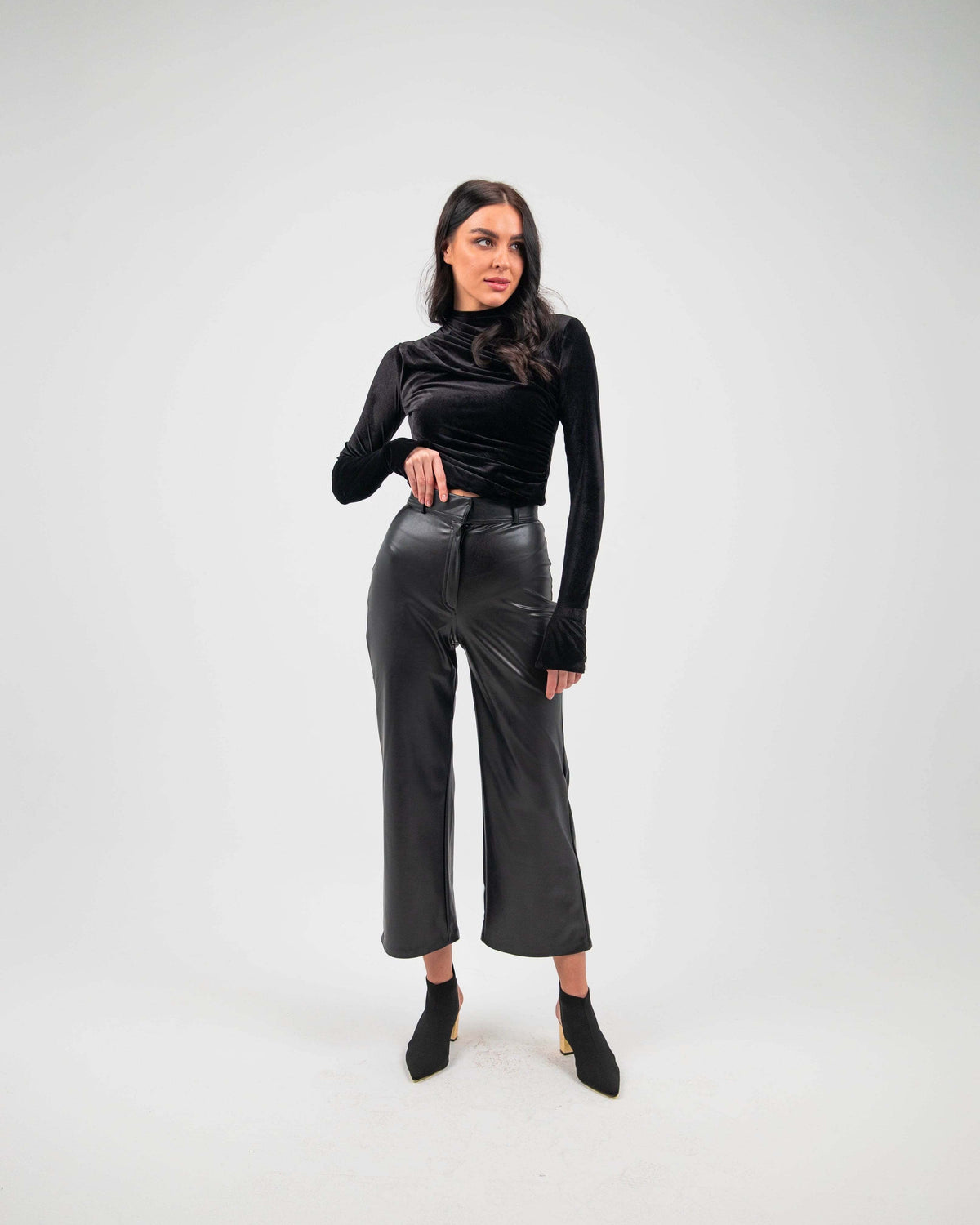 Woman wearing black straight leg faux leather pants and long sleeve black top, studio background