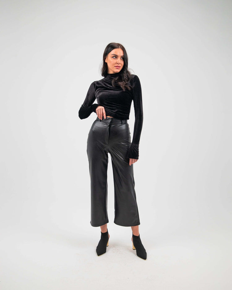 Woman wearing black straight leg faux leather pants and long sleeve black top, studio background
