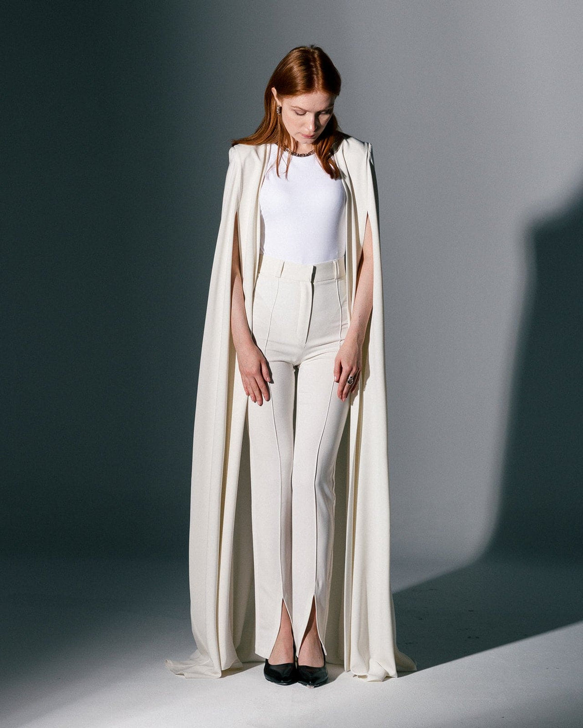 Woman wearing a cream crepe cape gown and tailored pants in a studio setting