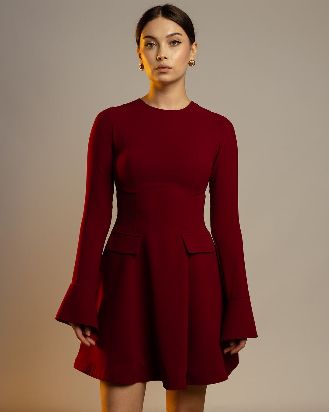 Woman wearing elegant long sleeve maroon dress with flared cuffs and A-line skirt