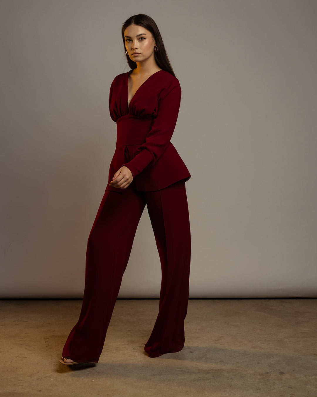 Woman wearing an elegant maroon wide-leg pantsuit with deep v-neck top, standing indoors