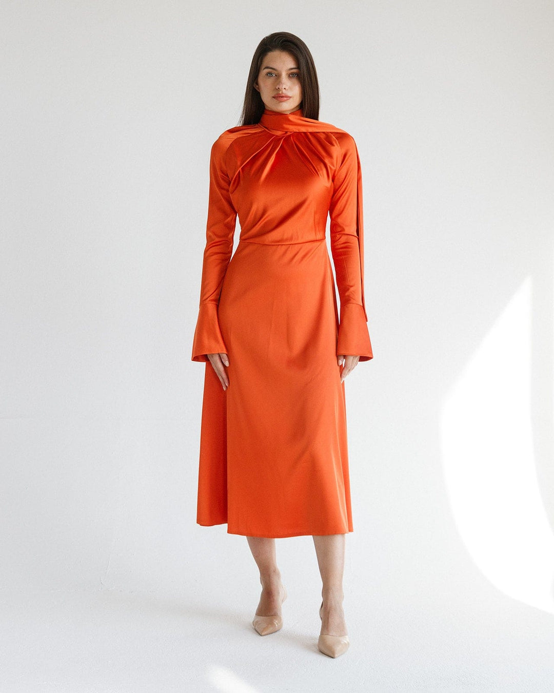 Woman in elegant long-sleeve orange satin midi dress with high neckline